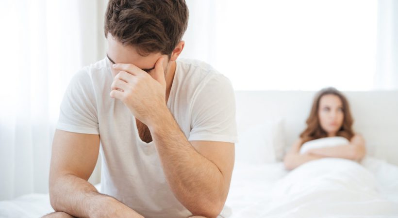 Depressed man sitting on bed and having problems with girlfriend